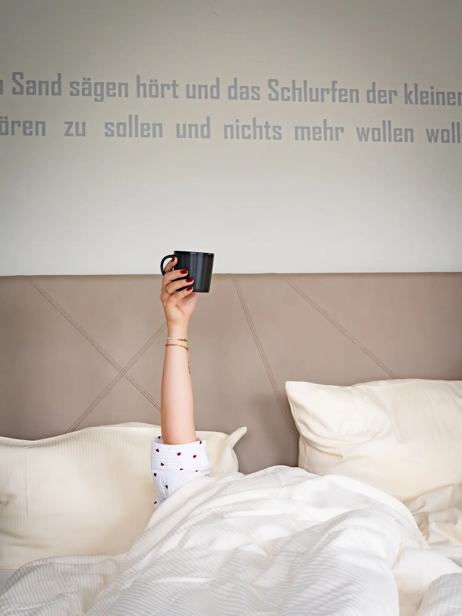 Jemand liegt unter der Bettdecke und hält eine Kaffeetasse in die Luft.